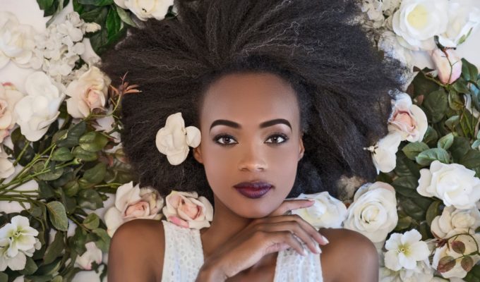 A black woman with makeup laying on flowers