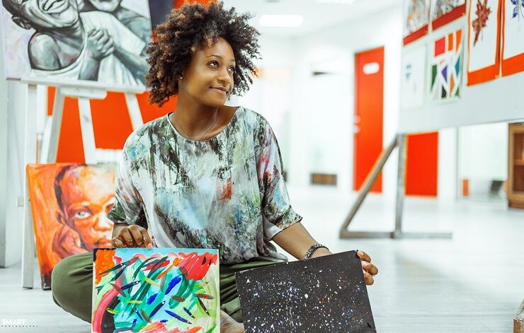 A Black woman sitting with two paintings made from self motivation