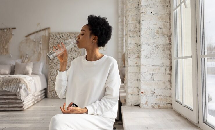 Black woman practicing morning rituals by drinking water in the morning