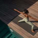 Woman practicing yoga in warrior two pose on a mat beside a pool, representing nervous system regulation through movement