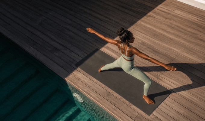 Woman practicing yoga in warrior two pose on a mat beside a pool, representing nervous system regulation through movement