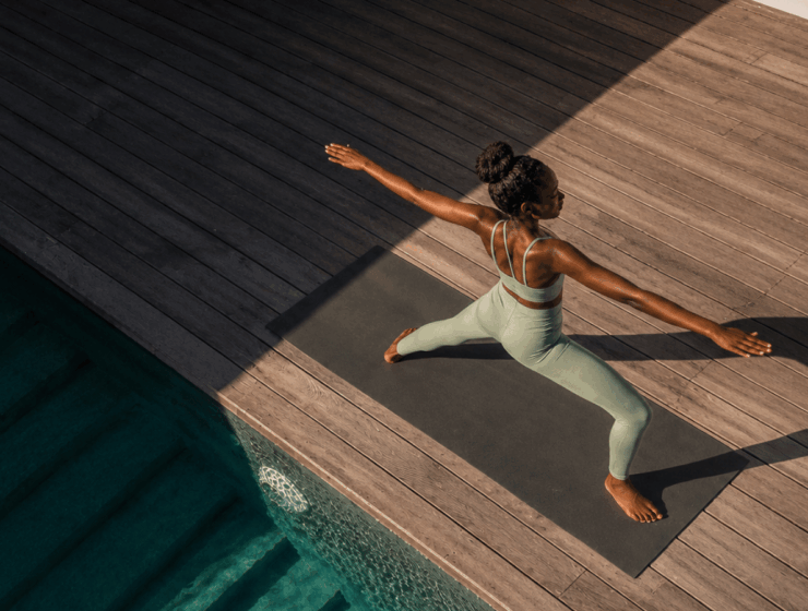 Woman practicing yoga in warrior two pose on a mat beside a pool, representing nervous system regulation through movement