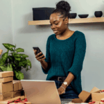African female entrepreneur managing customer orders from home while applying small business tips to improve productivity.