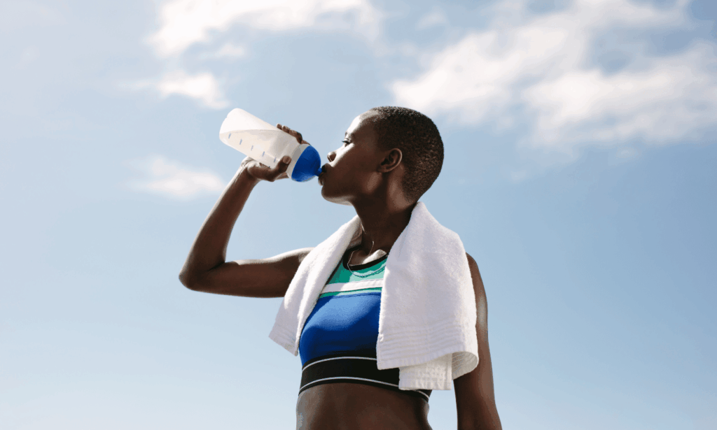 African woman drinking water after a workout, highlighting the benefits of drinking water for hydration and recovery.
