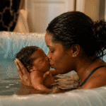 African mother kissing her newborn baby during a water birth in a birthing pool.