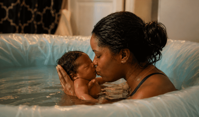 African mother kissing her newborn baby during a water birth in a birthing pool.