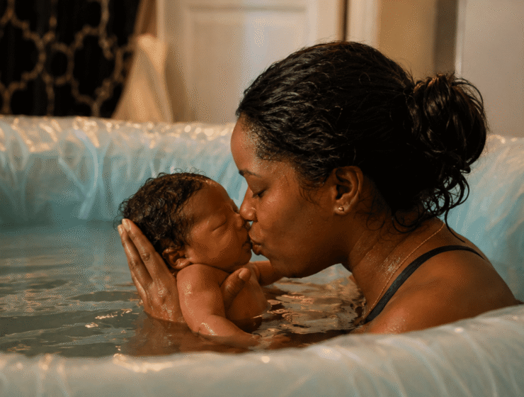 African mother kissing her newborn baby during a water birth in a birthing pool.