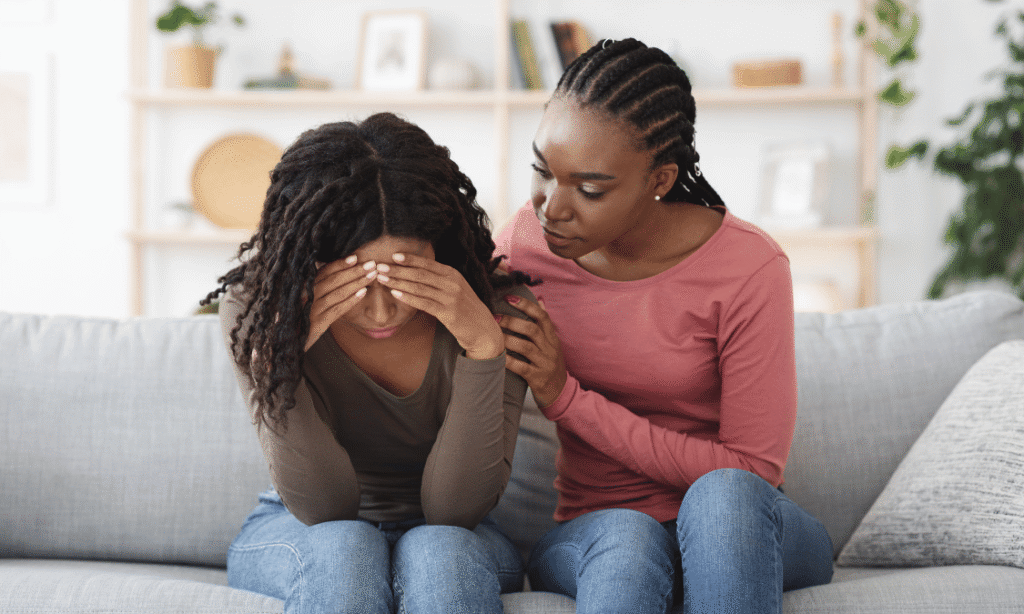 African woman comforting a distressed friend on a couch, reflecting the support at the heart of World Suicide Prevention Day