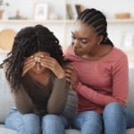 African woman comforting a distressed friend on a couch, reflecting the support at the heart of World Suicide Prevention Day