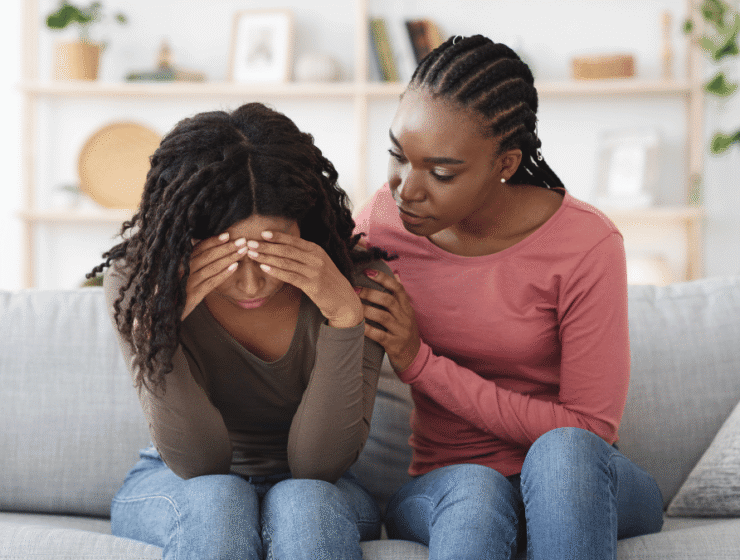 African woman comforting a distressed friend on a couch, reflecting the support at the heart of World Suicide Prevention Day
