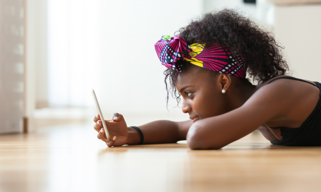 African woman lying on the floor checking her phone, illustrating one of the four attachment types.
