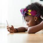 African woman lying on the floor checking her phone, illustrating one of the four attachment types.