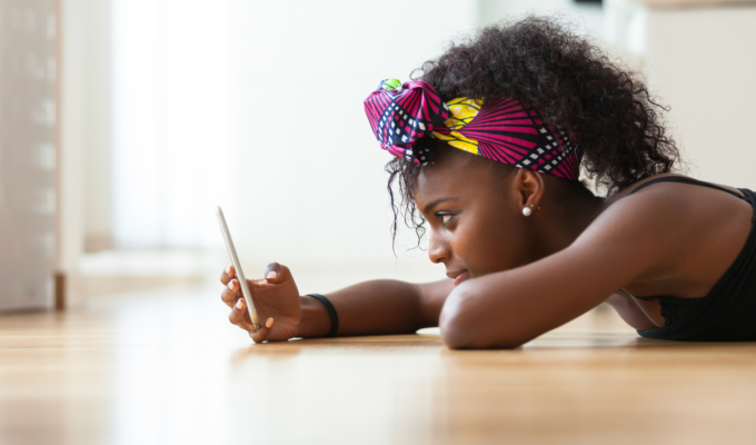 African woman lying on the floor checking her phone, illustrating one of the four attachment types.
